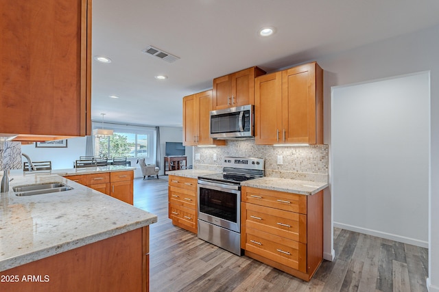 kitchen with light stone countertops, sink, stainless steel appliances, light hardwood / wood-style flooring, and kitchen peninsula