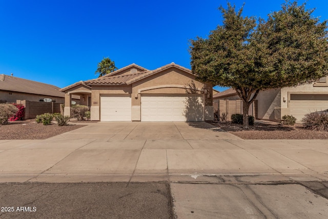 view of front facade with fence, concrete driveway, an attached garage, a tile roof, and stucco siding