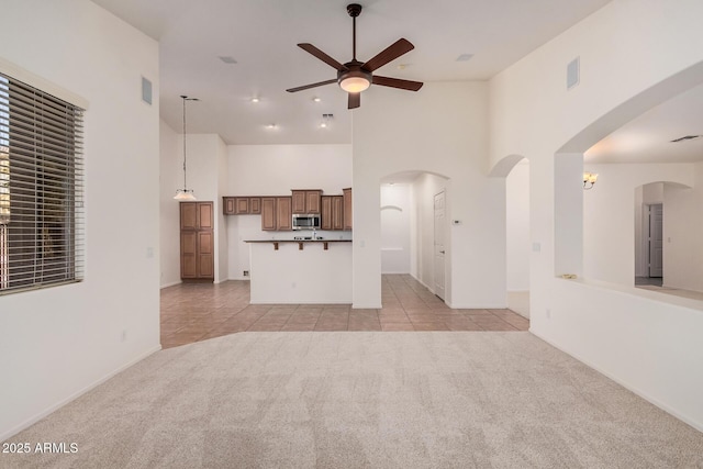 unfurnished living room with high vaulted ceiling, a ceiling fan, light colored carpet, and light tile patterned floors
