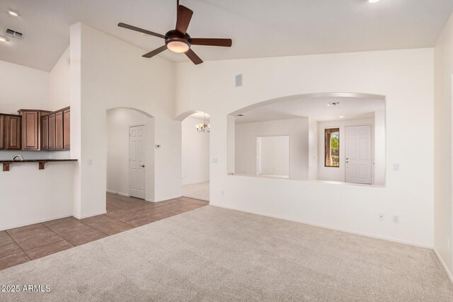 unfurnished living room featuring high vaulted ceiling, ceiling fan, carpet, tile patterned flooring, and visible vents