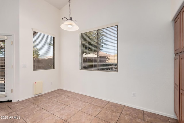 unfurnished dining area featuring a towering ceiling, baseboards, and light tile patterned floors