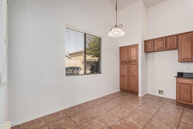 interior space with decorative light fixtures, brown cabinetry, a high ceiling, and baseboards