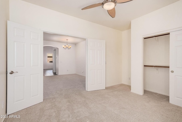 unfurnished bedroom featuring ceiling fan with notable chandelier, carpet flooring, arched walkways, and a closet