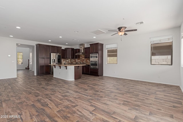 kitchen with a kitchen breakfast bar, wall chimney exhaust hood, open floor plan, and appliances with stainless steel finishes