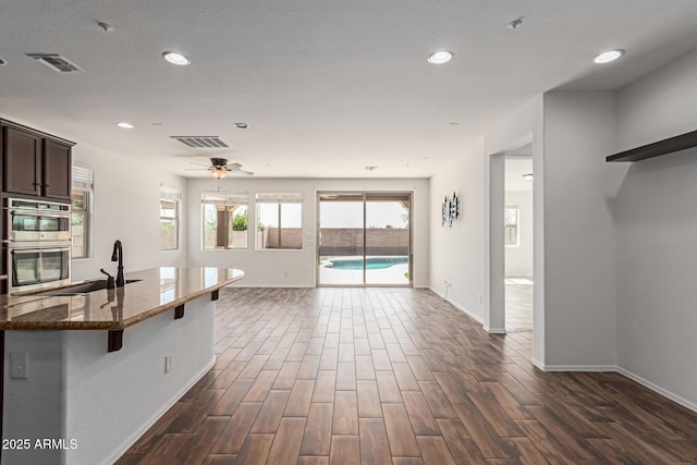 kitchen featuring visible vents, dark wood finished floors, open floor plan, dark stone counters, and stainless steel double oven