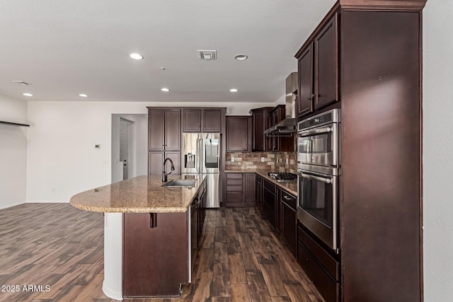 kitchen featuring visible vents, a sink, dark wood-type flooring, wall chimney range hood, and tasteful backsplash