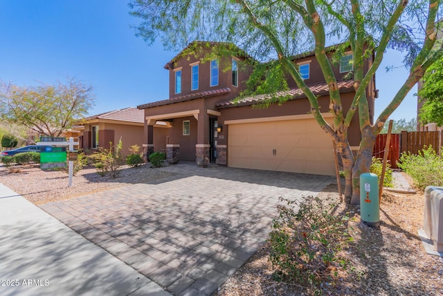 mediterranean / spanish house with fence, stucco siding, stone siding, a tiled roof, and decorative driveway