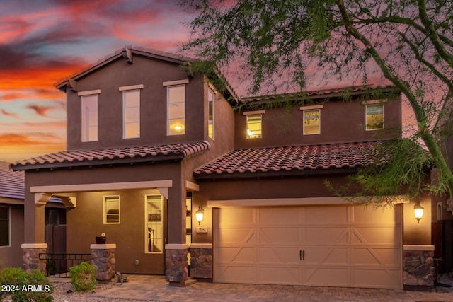 view of front of house with stucco siding, a garage, stone siding, a tile roof, and decorative driveway