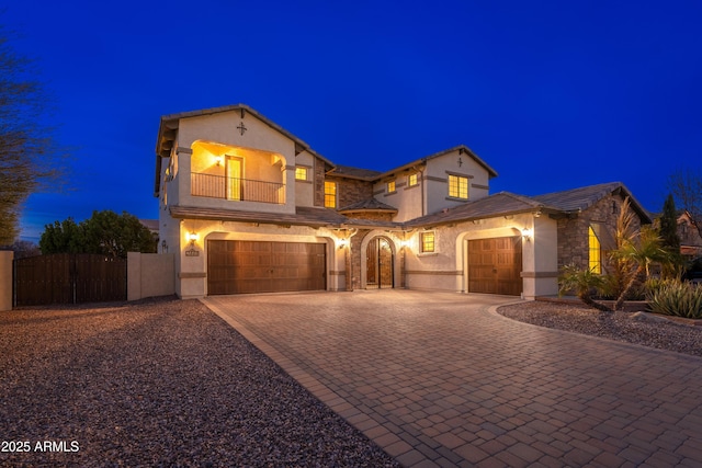 mediterranean / spanish-style house featuring stucco siding, a gate, decorative driveway, fence, and a balcony