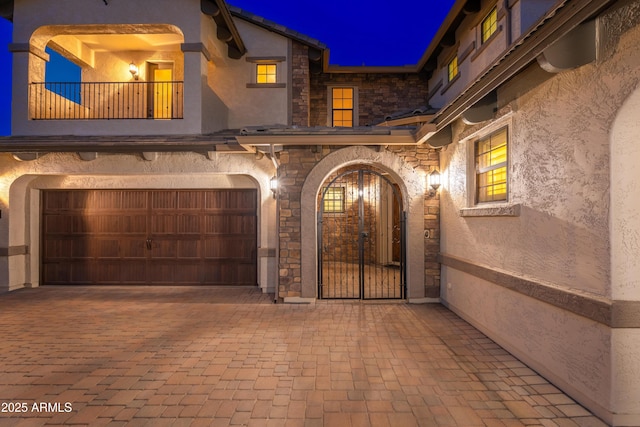 view of exterior entry with a balcony, a garage, stone siding, and stucco siding