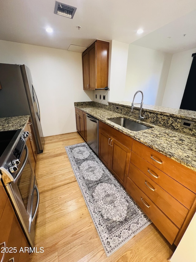 kitchen with stainless steel appliances, stone countertops, sink, and light hardwood / wood-style flooring