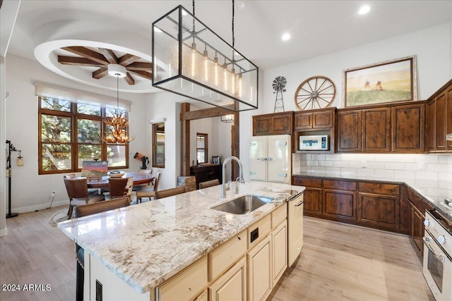 kitchen with a kitchen island with sink, a sink, light wood-style floors, white appliances, and ceiling fan with notable chandelier