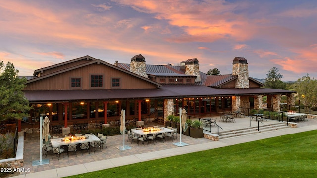 rear view of property with a standing seam roof, outdoor dining space, a chimney, and a patio area