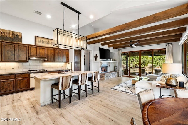 kitchen with a kitchen breakfast bar, a sink, open floor plan, light wood-type flooring, and a kitchen island with sink