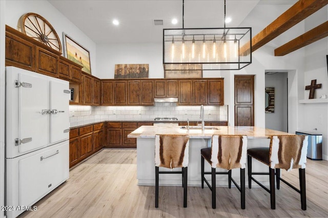 kitchen with light stone countertops, under cabinet range hood, light wood-style flooring, and a sink