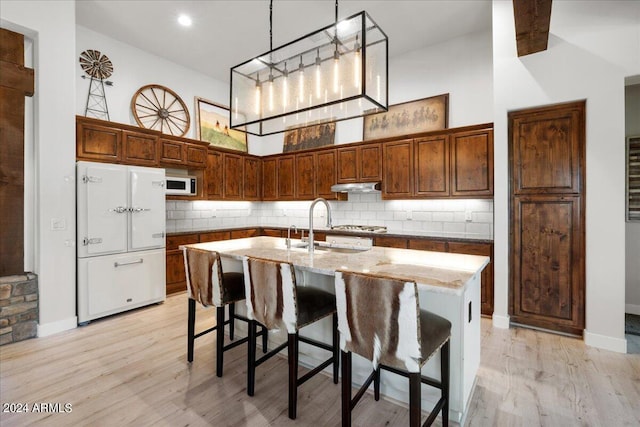kitchen with a high ceiling, a sink, under cabinet range hood, light stone counters, and white appliances