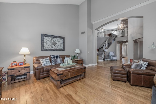 9708 E Pampa Ave, Mesa, AZ 85212 - living room featuring arched walkways, a towering ceiling, a chandelier, stairway, and light wood-style flooring