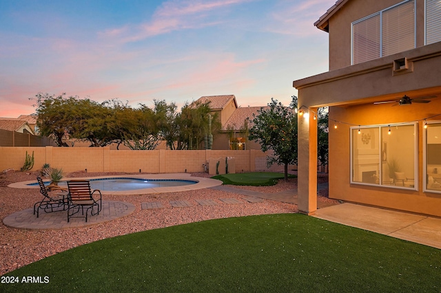 pool at dusk with a patio, ceiling fan, and a lawn