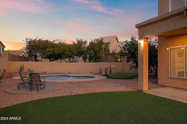 pool at dusk featuring a lawn and a patio