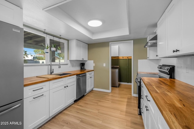 kitchen featuring a sink, a raised ceiling, stainless steel appliances, washer / dryer, and butcher block counters