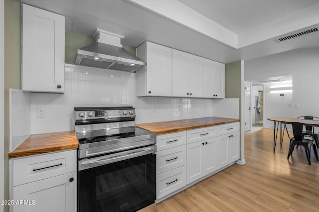 kitchen featuring wooden counters, white cabinetry, wall chimney exhaust hood, and stainless steel range with electric cooktop