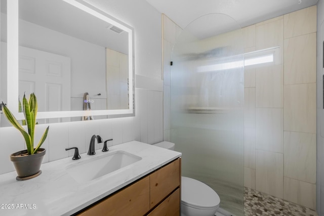 bathroom with visible vents, tile walls, a tile shower, vanity, and toilet