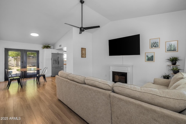 living room featuring light wood-style floors, a glass covered fireplace, lofted ceiling, and ceiling fan