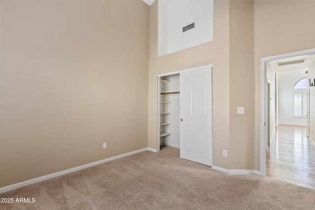 unfurnished bedroom featuring a high ceiling, light carpet, and a closet