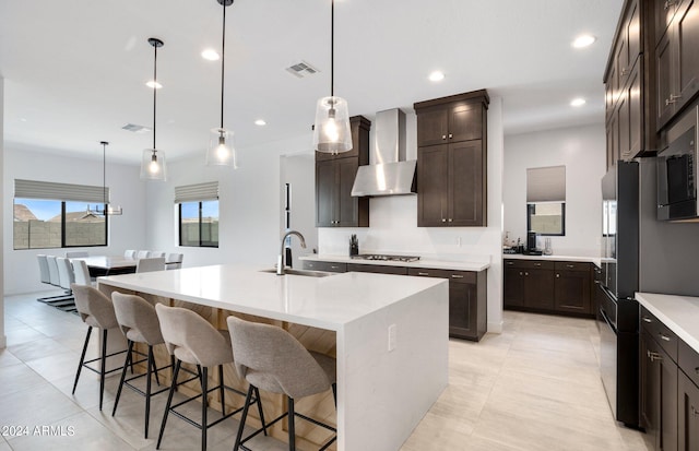 kitchen featuring wall chimney exhaust hood, sink, decorative light fixtures, and a center island with sink