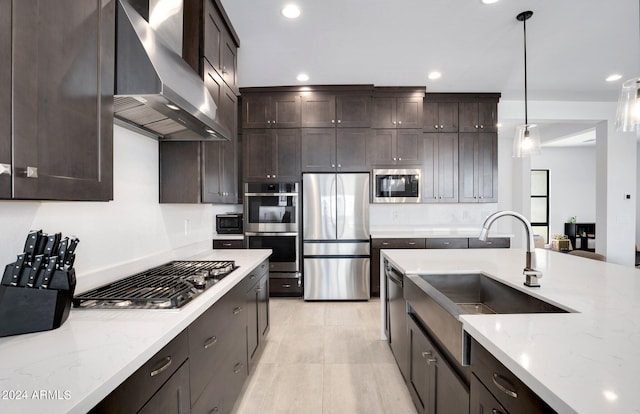 kitchen featuring appliances with stainless steel finishes, light stone countertops, wall chimney exhaust hood, dark brown cabinetry, and decorative light fixtures