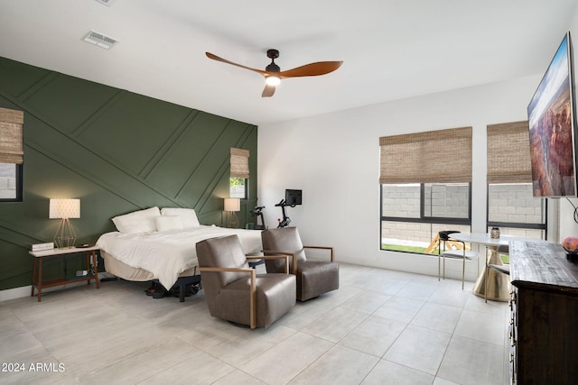 bedroom with a ceiling fan, visible vents, light tile patterned floors, and a decorative wall
