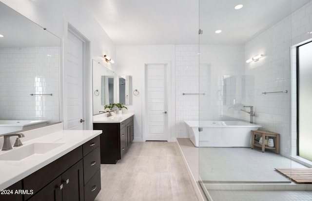 full bath with a sink, a freestanding tub, two vanities, and tile walls