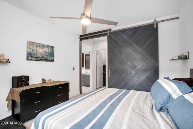 bedroom with connected bathroom, a barn door, light colored carpet, and ceiling fan