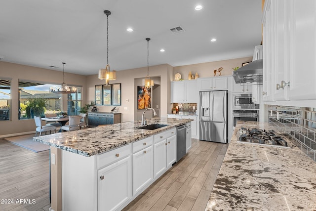 kitchen featuring white cabinetry, appliances with stainless steel finishes, wall chimney exhaust hood, and a center island with sink