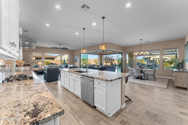 kitchen with a center island with sink, wall chimney exhaust hood, white cabinetry, and plenty of natural light