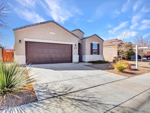 mediterranean / spanish house featuring an attached garage, fence, driveway, a tiled roof, and stucco siding