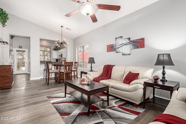 living room featuring dark wood-style flooring, visible vents, vaulted ceiling, baseboards, and ceiling fan with notable chandelier