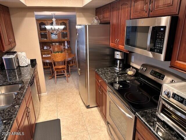 kitchen featuring stainless steel appliances, a raised ceiling, light tile patterned floors, a notable chandelier, and hanging light fixtures