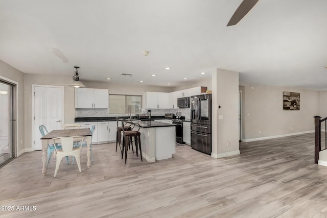 kitchen featuring tasteful backsplash, stainless steel microwave, refrigerator with ice dispenser, light wood-style floors, and white cabinets