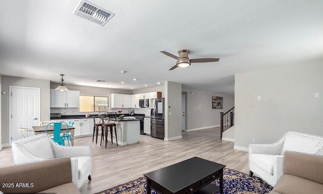 living area with visible vents, a ceiling fan, stairway, light wood-style floors, and baseboards