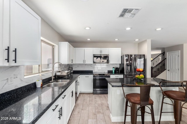 kitchen featuring visible vents, appliances with stainless steel finishes, a kitchen breakfast bar, white cabinets, and a sink