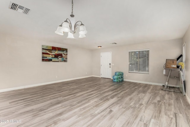 unfurnished living room featuring visible vents, baseboards, an inviting chandelier, and wood finished floors