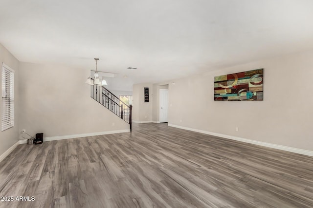 unfurnished living room with a wealth of natural light, a notable chandelier, stairs, and wood finished floors