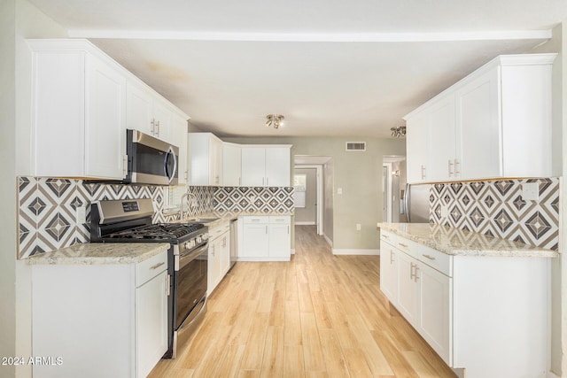 kitchen featuring light stone countertops, light hardwood / wood-style flooring, decorative backsplash, white cabinets, and appliances with stainless steel finishes