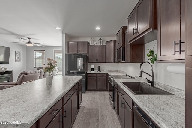 kitchen featuring dark brown cabinetry, appliances with stainless steel finishes, open floor plan, light wood-type flooring, and a sink