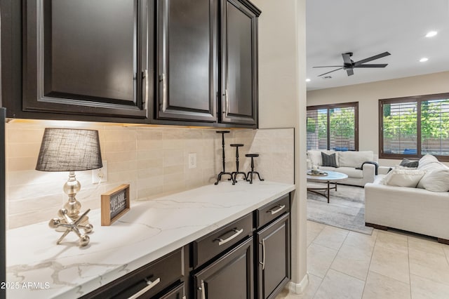 kitchen featuring open floor plan, decorative backsplash, a ceiling fan, light stone counters, and light tile patterned floors