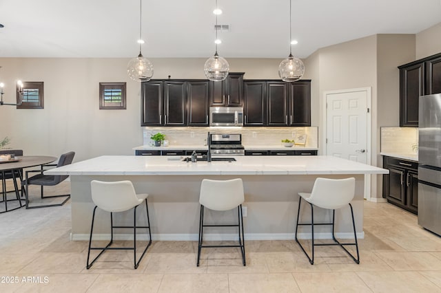 kitchen with stainless steel appliances, tasteful backsplash, a sink, a center island with sink, and a breakfast bar area