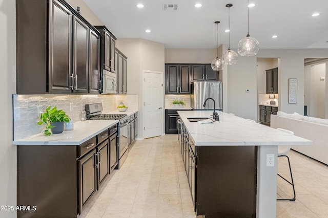 kitchen with stainless steel appliances, a sink, decorative backsplash, recessed lighting, and an island with sink