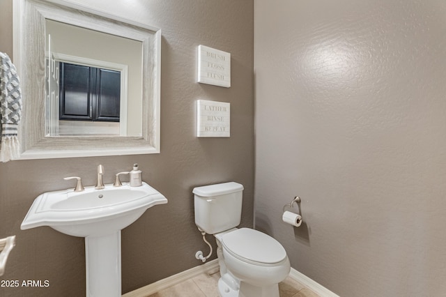 half bathroom with toilet, baseboards, and tile patterned floors
