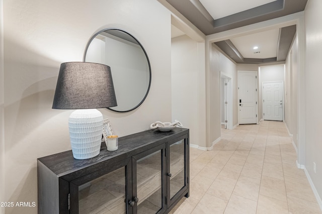 hall featuring a tray ceiling and baseboards